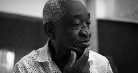 One Elderly Afro-descendant man in black and white portrait, looking upwards with a thoughtful smile, hand touching chin, facial features highlighted in a serene outdoor home setting