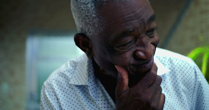 One Elderly Afro-descendant man with a pensive and slightly concerned expression, hand resting on chin, engaging in deep thought in a serene home environment
