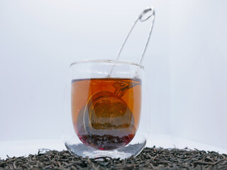 Glass Cup of Black Tea with Infuser and Loose Leaves on White Background