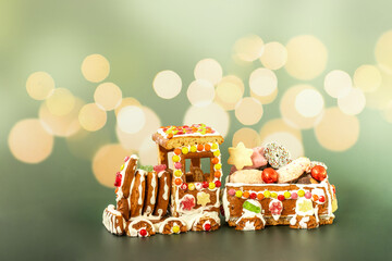 Handcrafted gingerbread train decorated with icing, candy, and cookies, filled with festive sweets and chocolate balls, displayed on a green background in cheerful Christmas style