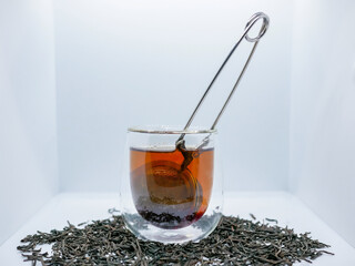 Glass Cup of Black Tea with Infuser and Loose Leaves on White Background