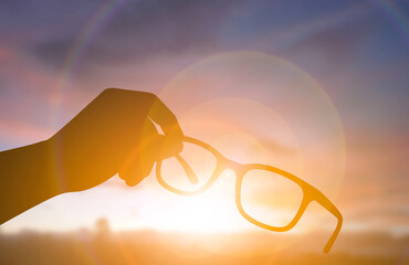 Silhouette hand holding eyeglasses against bright sunset light