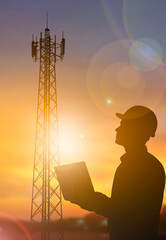 Silhouette engineer checking communication tower with laptop at sunset