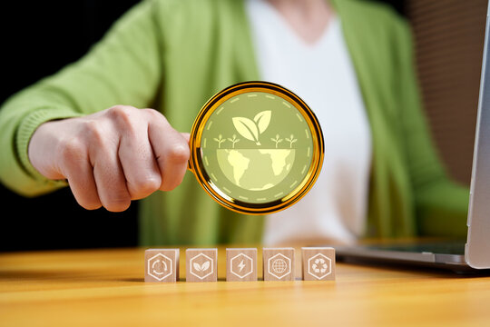 Businesswoman analyzing sustainability icons with magnifying glass. Concept of ESG, green business, environmental responsibility, renewable energy, recycling, and corporate sustainability audit.