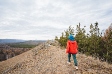 Naklejka premium Young man on mountain trail, Young person walks along solitary mountain ridge at dusk, Caucasian teenage boy carefully navigates narrow ridge through peaceful valley scenery with overcast