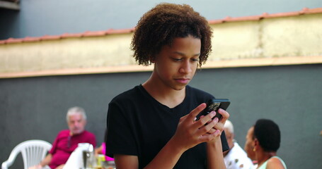 Teenager using smartphone outdoors, focused and serious, with a casual social atmosphere and...