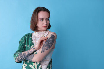 Young woman with piercings, tattoos and stylish clothes posing on light blue background, space for text