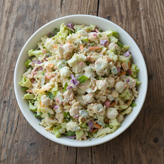 A fresh summer coleslaw salad with light yogurt dressing served in a white bowl on a textured wooden table.