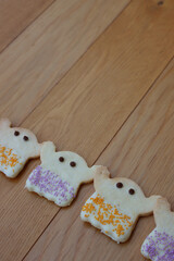 Halloweeen shortcrust cookies in shape of a ghost with white chocolate glaze and colorful sprinkles in a row   on wooden table with copy space