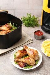 Air fryer with grilled chicken drumsticks and french fries on grey table