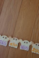 Halloweeen shortcrust cookies in shape of a ghost with white chocolate glaze and colorful sprinkles in a row   on wooden table with copy space