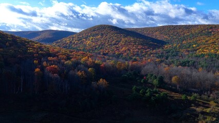 Mountains and hills in beautiful Autumn Fall colors at Tioga, Pennsylvania countryside in morning sunlight with blue sky and white clouds overhead
