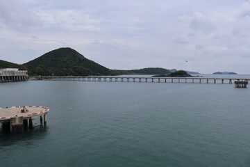 Obraz premium A serene coastal scene with a calm sea under an overcast sky. On the left side of the image, there's a dock extending into the water