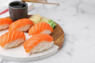 Delicious nigiri sushi with salmon, wasabi, ginger and soy sauce on white marble table, closeup. Space for text