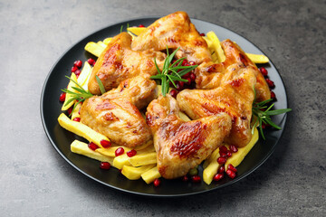 Delicious grilled chicken wings with french fries, pomegranate seeds and rosemary on grey table, closeup