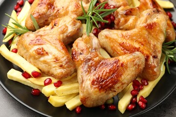 Delicious grilled chicken wings with french fries, pomegranate seeds and rosemary on grey table, closeup