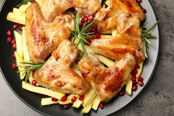 Delicious grilled chicken wings with french fries, pomegranate seeds and rosemary on grey table, top view
