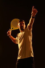 Player in a white shirt serves with a paddle in a dramatic spotlight during a match