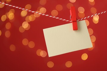 Blank card hanging on string against red background, bokeh effect. Mockup for design