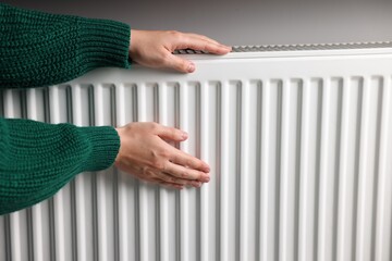 Woman warming her hands near radiator indoors, closeup. Space for text