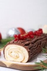 Delicious Yule log (traditional Christmas cake) with redcurrant and fir tree branches on light table, closeup