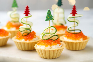 Christmas food. Tasty tartlets with red caviar, cream cheese, cucumber and decor on table against...