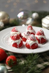 Christmas food. Santa hats made of strawberries, whipped cream and decor on table against background with blurred lights, closeup. Bokeh effect
