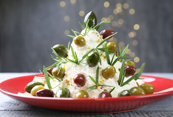 Delicious Christmas tree cheese ball with olives and rosemary on wooden table against grey background with blurred lights, closeup. New Year's appetizer