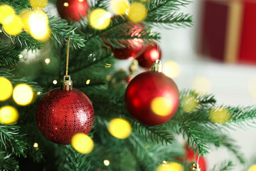 Christmas baubles hanging on fir tree branches against blurred background, closeup. Bokeh effect