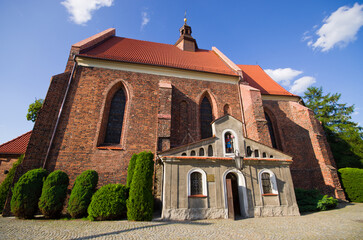 Fototapeta premium Historic brick church with red tiled roof under blue sky, Ostrzeszow, Poland