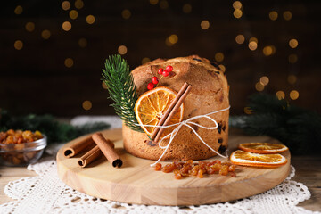Christmas food. Delicious Panettone cake, ingredients and festive decor on wooden table against background with blurred lights, closeup. Bokeh effect