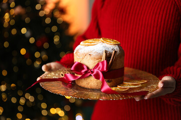 Christmas food. Woman with delicious Panettone cake against background with blurred lights,...