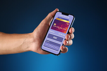 Online payment. Man holding mobile phone with open app in hand on blue background, closeup