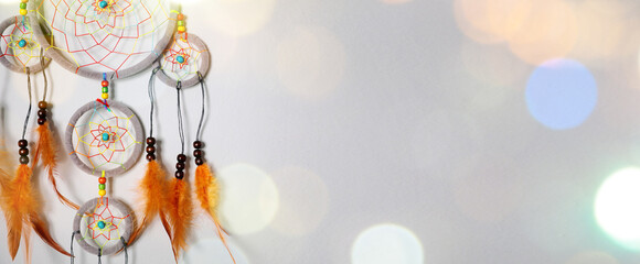 Dream catcher with feathers on light background, bokeh lights. Banner design