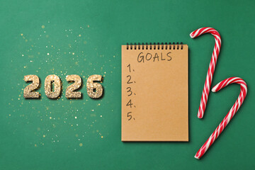 New 2026 Year Goals. Inscription in notebook, candy canes and numbers on green background, top view