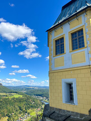 Yellow historic building on a hill with bright blue sky and panoramic valley view.