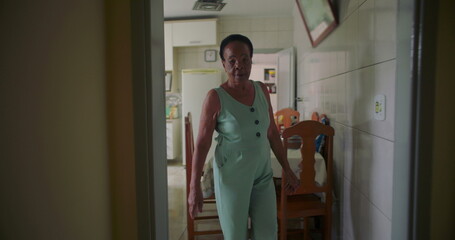 Fototapeta premium Elderly African American woman walking through a corridor at home, transitioning from the kitchen to the living room, reflecting introspection and a quiet, reflective moment