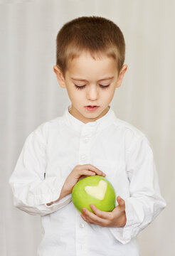 Close-up portrait of a young boy in a white shirt holding a green apple with a missing bite in the shape of a heart