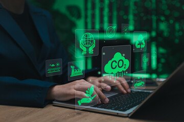 Carbon footprint and sustainability concept. Person using laptop with green icons of CO2 reduction, clean energy, recycling, eco-friendly tech, symbolizing climate action, environmental responsibility