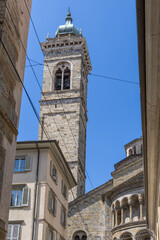 The stone bell tower of Saint Mary Major Basilica in Bergamo Italy stands tall beside the Romanesque apse, its aged walls and greenish dome glowing in bright midday sunlight