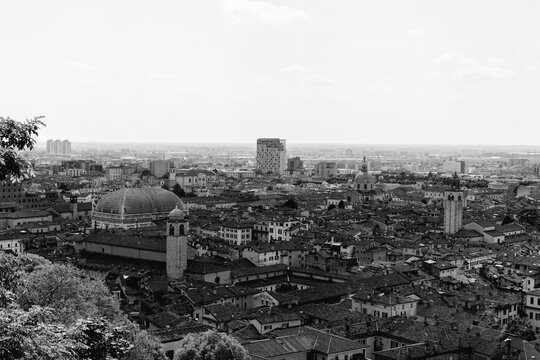 Historic skyline of Brescia with bell towers, tiled roofs, and Renaissance domes contrasting with modern buildings on the distant horizon