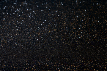 Macro black textured surface with golden glitter in sharp focus at bottom, sparkling grains create cosmic starry illusion blending into soft blur above