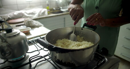 Close-up of a woman stirring rice in a pot on a stovetop, capturing the essence of home cooking, warmth, and tradition in an intimate kitchen setting