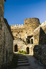 Fototapeta premium Interior courtyard of Ananuri fortress with medieval stone walls, arched doors and a round defensive tower under clear blue sky