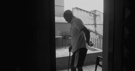 Fototapeta premium Elderly man stepping into the porch with a cane, silhouetted in black and white, symbolizing resilience, independence, and reflection in a serene outdoor moment