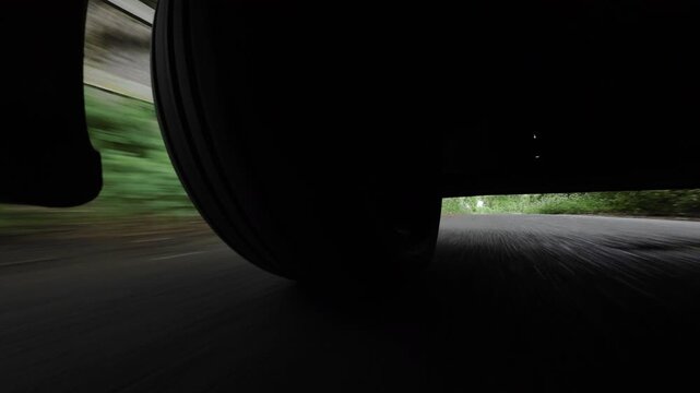 Low-mounted action-camera view beneath a car driving along a tree-shaded country road near Sevenoaks, Kent, United Kingdom, turning a corner and passing a parked car.