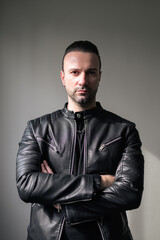 Obraz premium Portrait of a handsome young man in black leather jacket with arms crossed