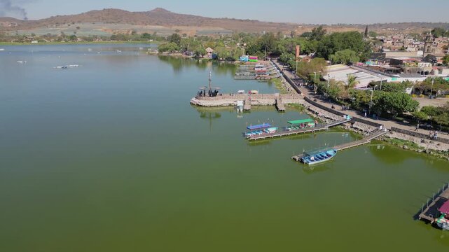 Aerial forward shot starting above the lake and approaching the Cajititlan malecon with colorful boats