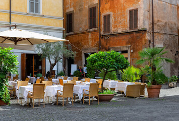 View of old narrow street with tables of restaurant in Rome, Italy. Architecture and landmark of Rome. Cozy cityscape of Rome.