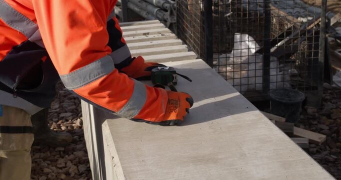 Worker in high-visibility gear writes identification and measurements on a structural concrete column at a construction site. 